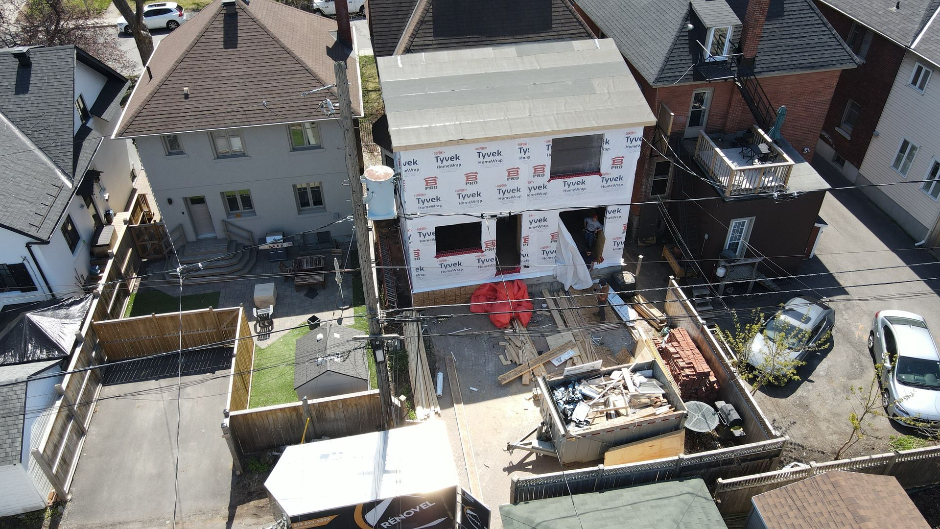 Vue aérienne d'une maison en rénovation, mitoyenne de plusieurs maisons, avec des échafaudages, des débris et un salon de jardin rouge.