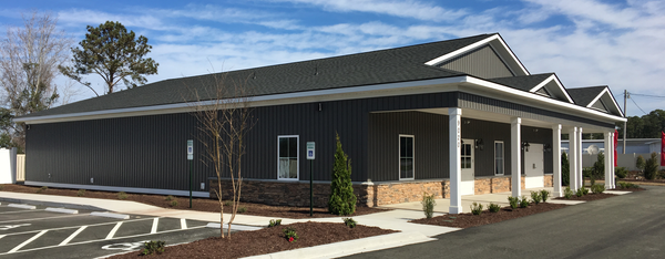 A modern, dark-gray, single-story commercial building with a stone-accented base, white columns, and a parking lot.
