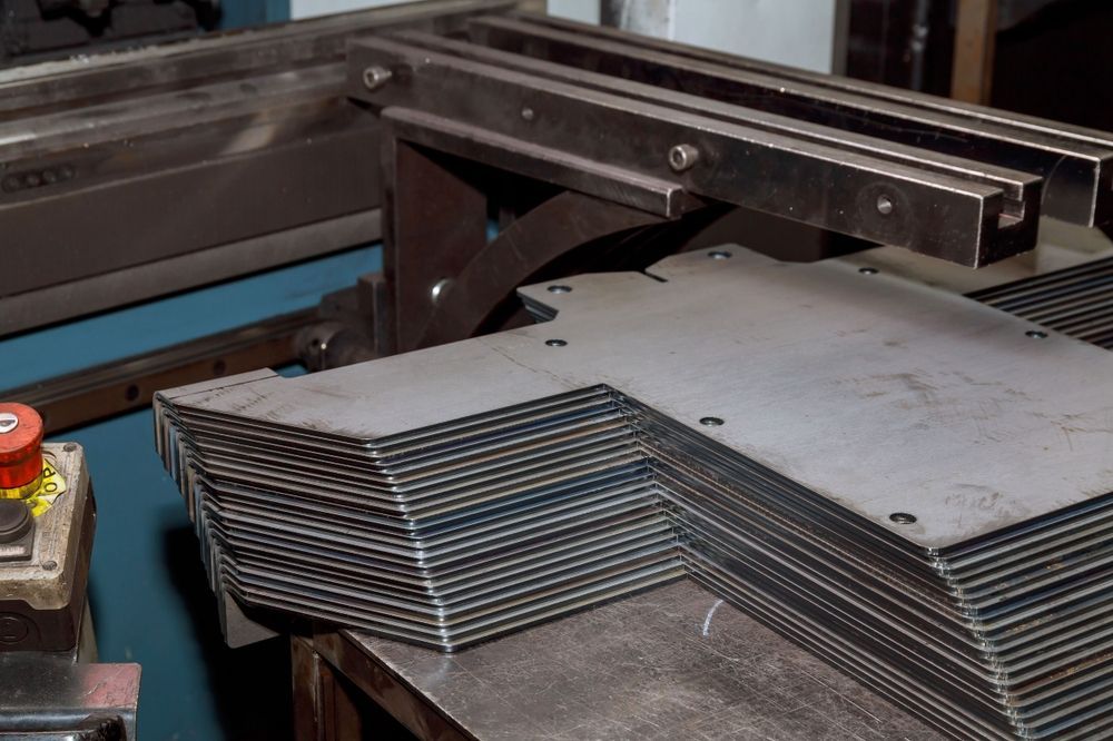 A stack of cut metal sheets with an L-shaped design, beside a metal working machine — Townsville Stainless Steel in Hughenden, QLD