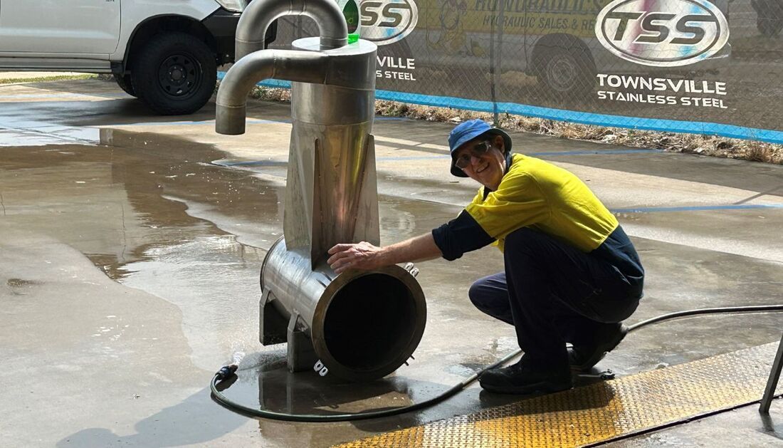 A Man Is Kneeling Down Next to A Large Metal Pipe — Townsville Stainless Steel in Garbutt, QLD A Man Is Kneeling Down Next to A Large Metal Pipe — Townsville Stainless Steel in Garbutt, QLD
