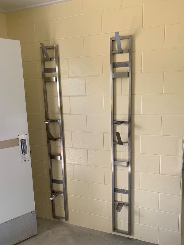 Two Metal Ladders Are Hanging on A Yellow Brick Wall — Townsville Stainless Steel in Garbutt, QLD Two Metal Ladders Are Hanging on A Yellow Brick Wall — Townsville Stainless Steel in Garbutt, QLD