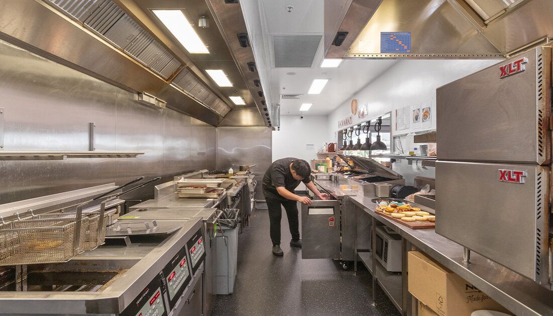 A Man Is Standing in A Long Kitchen Preparing Food — Townsville Stainless Steel in Garbutt, QLD