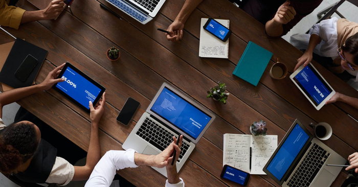 A group of people are sitting around a table with laptops and tablets.