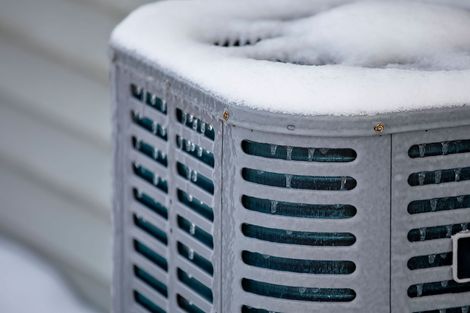 An outdoor air conditioning unit covered in ice and snow, with icicles hanging from its metal casing.