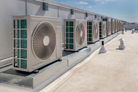 A row of light-colored HVAC outdoor units lined up on a building rooftop against a blue sky.