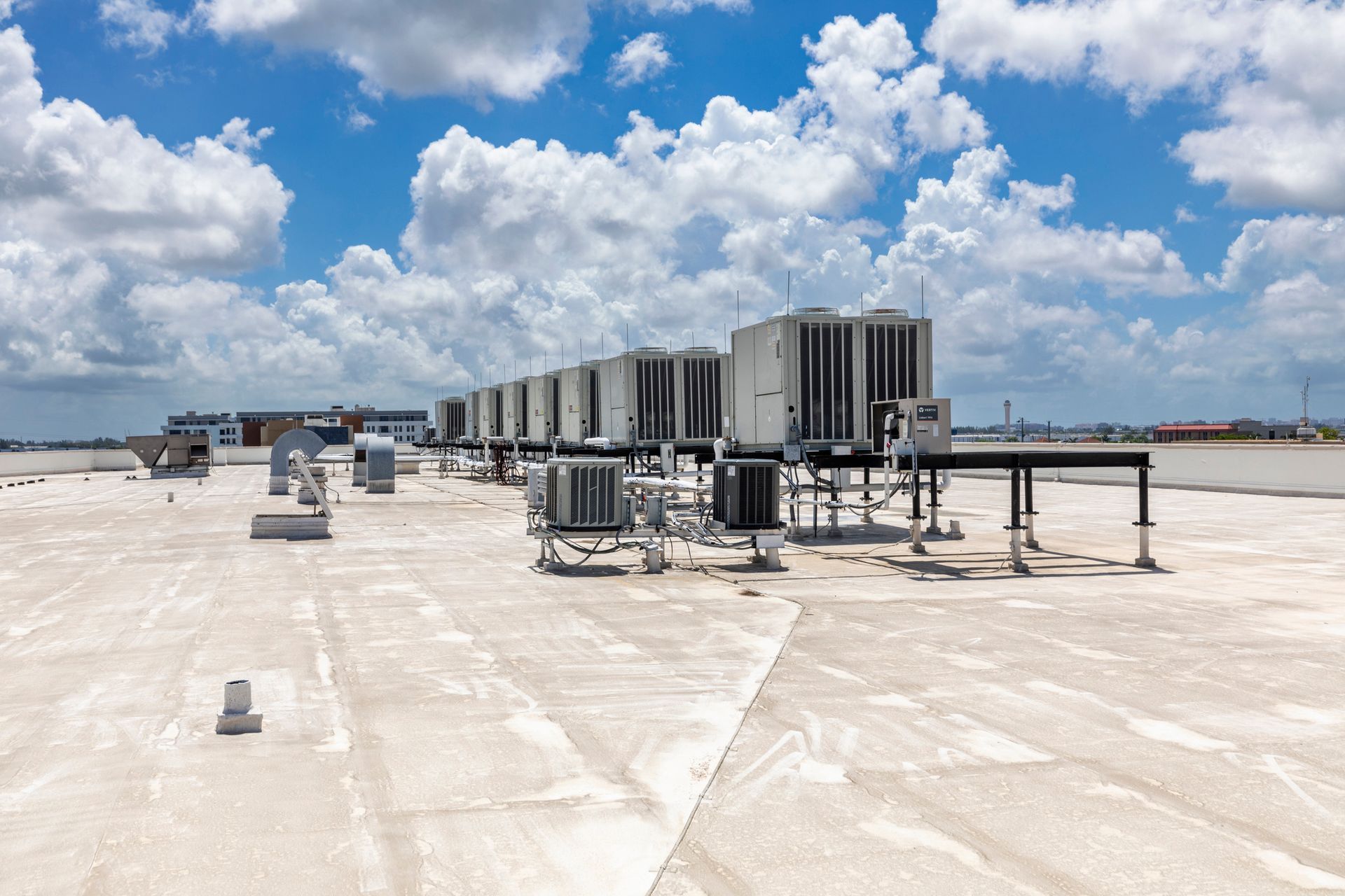 A row of industrial HVAC units on a flat rooftop under a blue sky with scattered clouds.