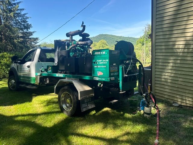 Green utility truck with vacuum equipment parked on a grassy yard beside a house on a sunny day