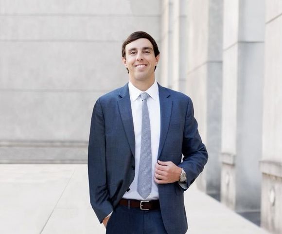 Man in a blue suit smiling outdoors beside a stone building
