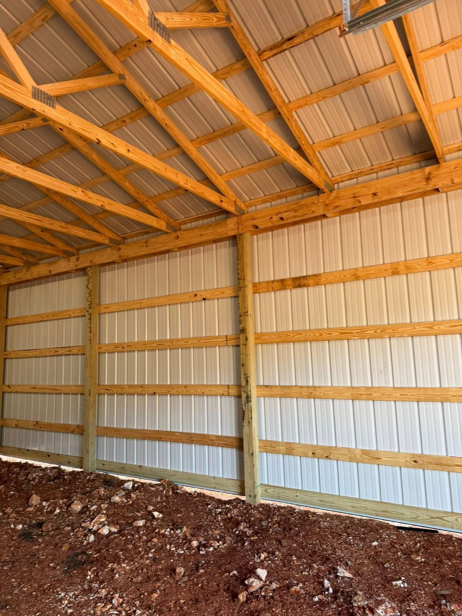 Interior of a barn with corrugated metal walls, wooden beams, and a dirt floor.