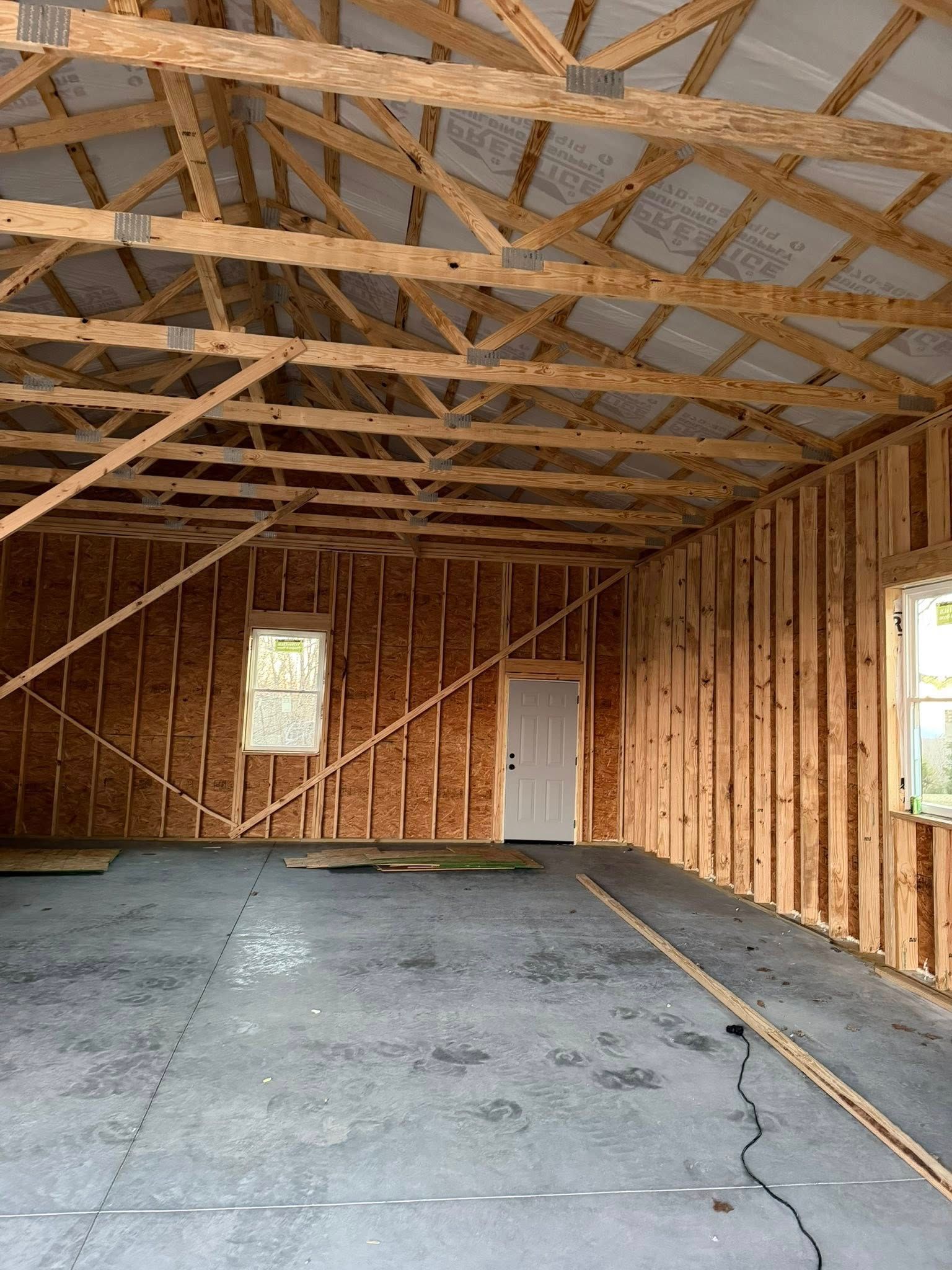 Interior of unfinished wood-framed building with concrete floor, exposed trusses, and windows