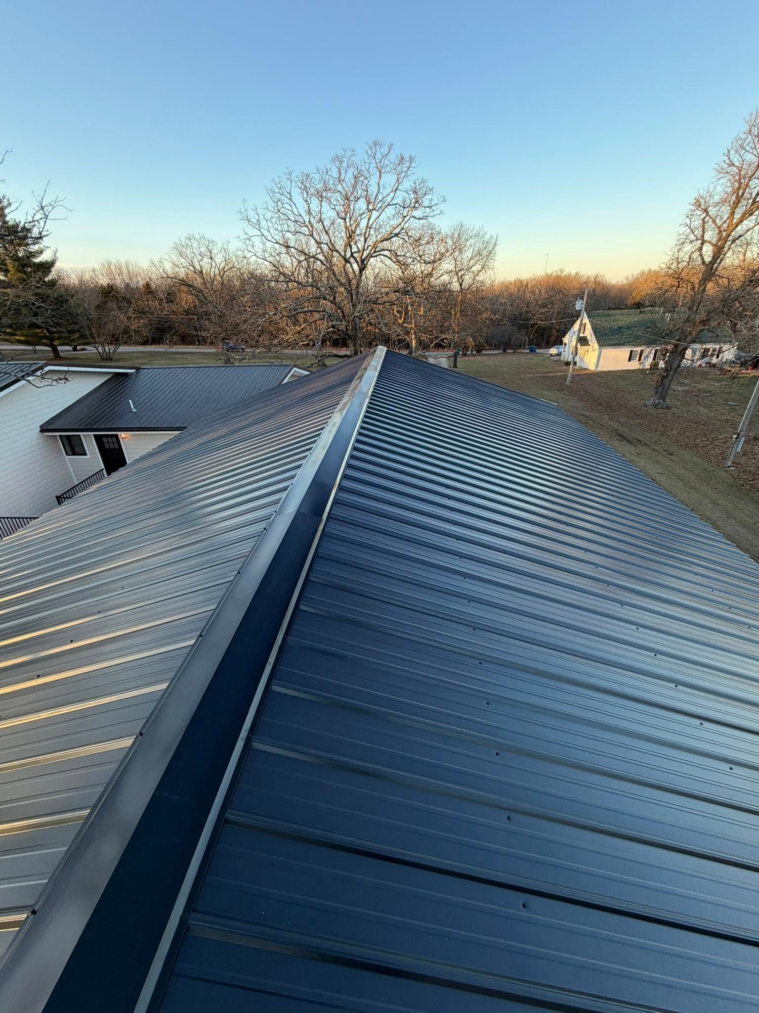 Curved blue metal rooftop at sunset with trees and a clear sky in the background