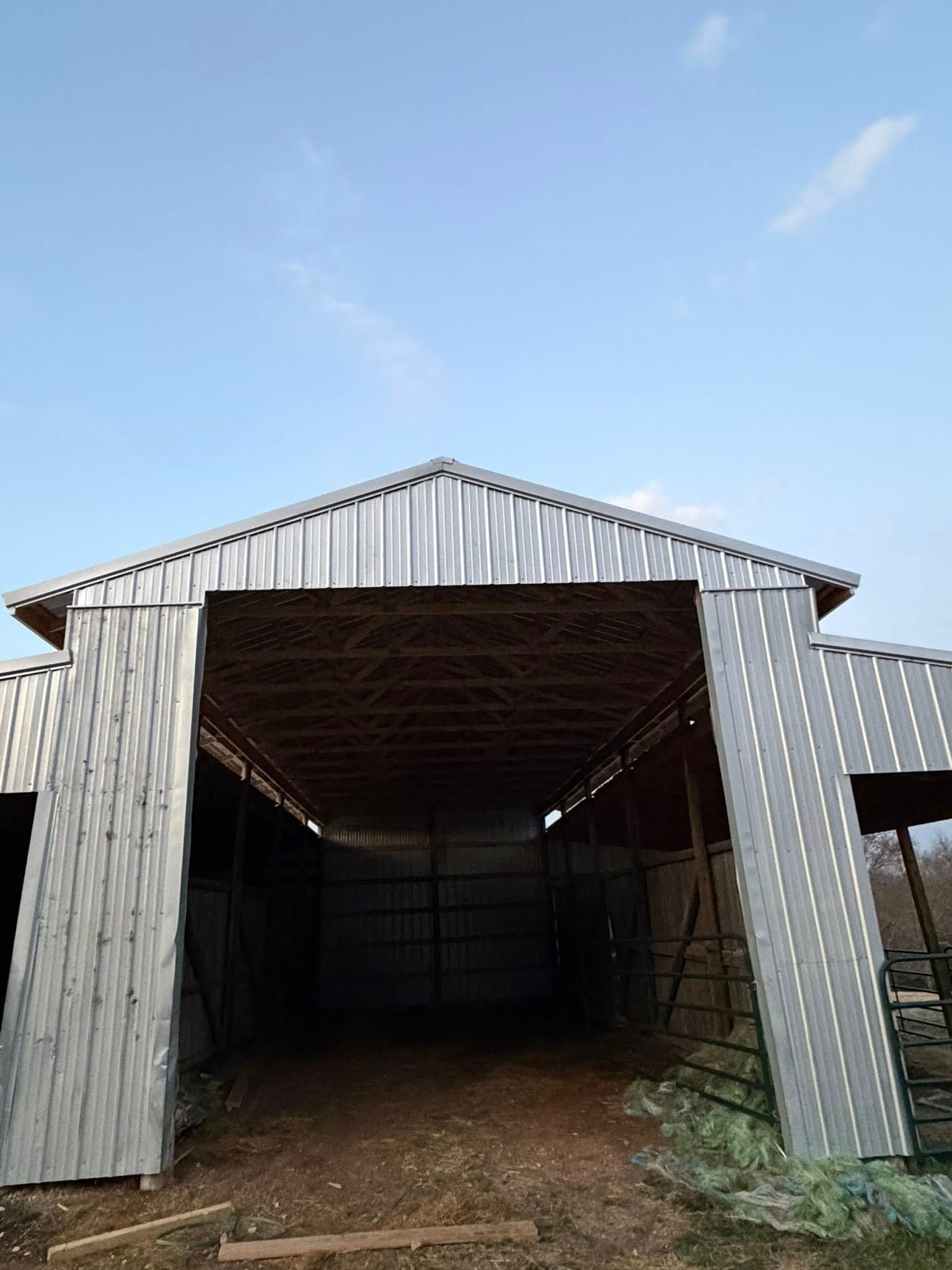Open metal barn with corrugated walls and roof, viewed from the entrance under a blue sky.