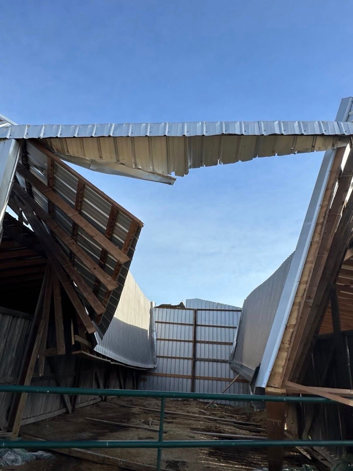 Collapsed metal roof over a damaged structure, with twisted panels against a blue sky