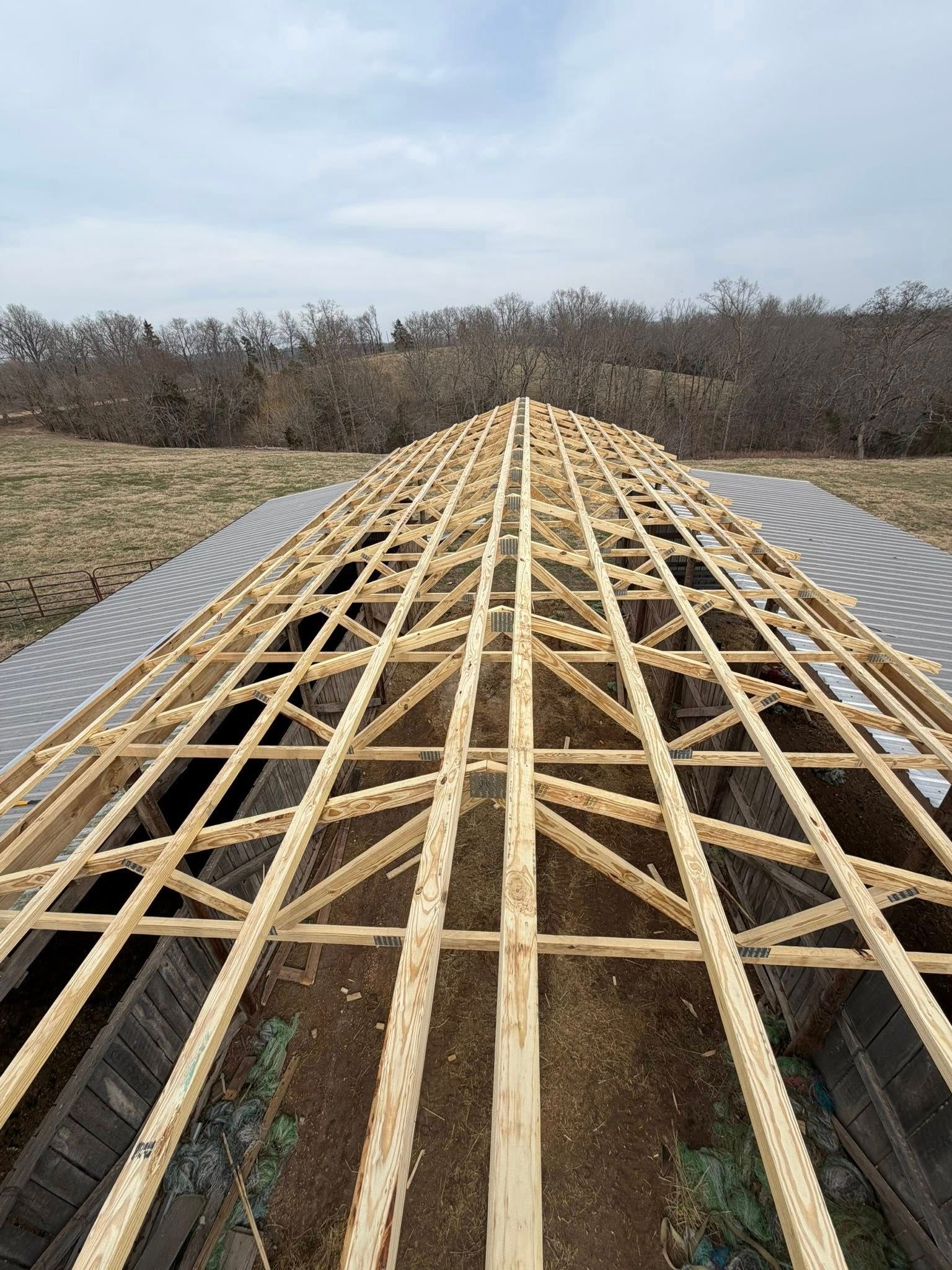 Long wooden lattice walkway under construction across a grassy field, viewed from the centerline