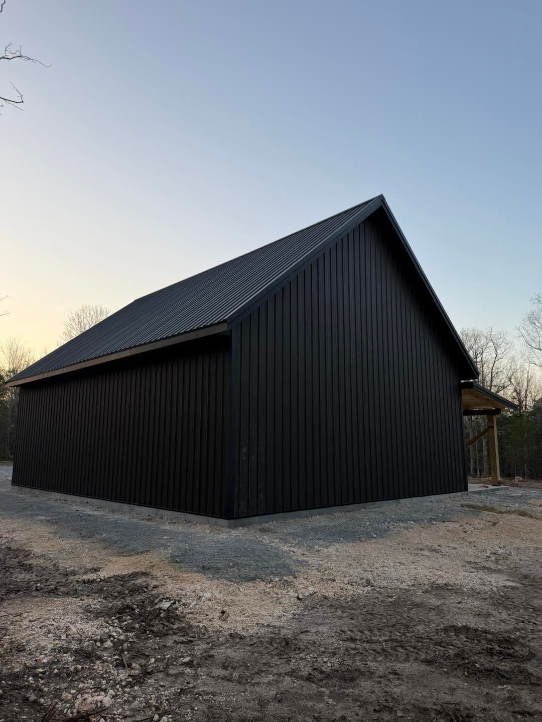 Black corrugated-metal barn with steep roof on gravel at sunset