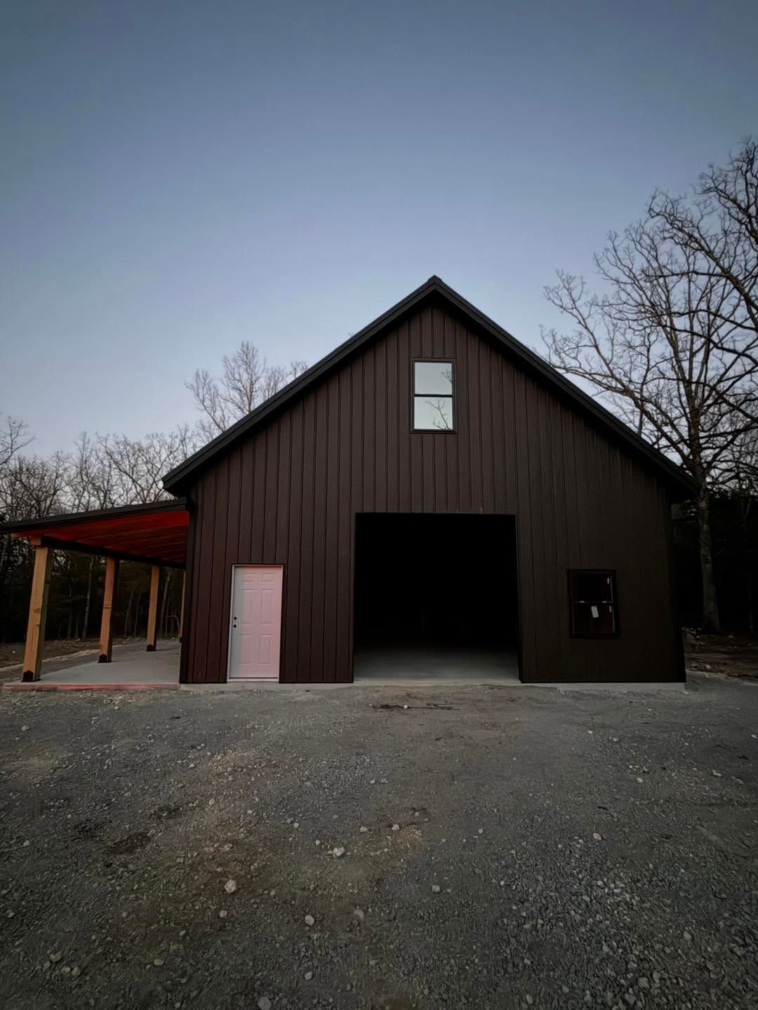 Dark brown barn with open doorway and pink door, on a gravel lot at dusk.