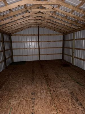 Empty interior of a metal storage shed with plywood floor and exposed wooden roof trusses.