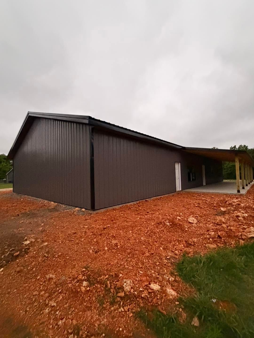 Brown metal building on a red dirt lot under an overcast sky
