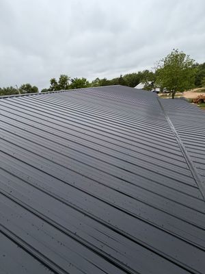 Black ribbed metal roof under cloudy sky with trees in the background