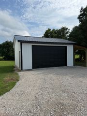 Small white garage with black door on gravel driveway under a cloudy sky