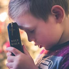 A young boy, eyes closed, holds a Holy Bible with a gold cross on the cover close to his face. A young boy, eyes closed, holds a Holy Bible with a gold cross on the cover close to his face.