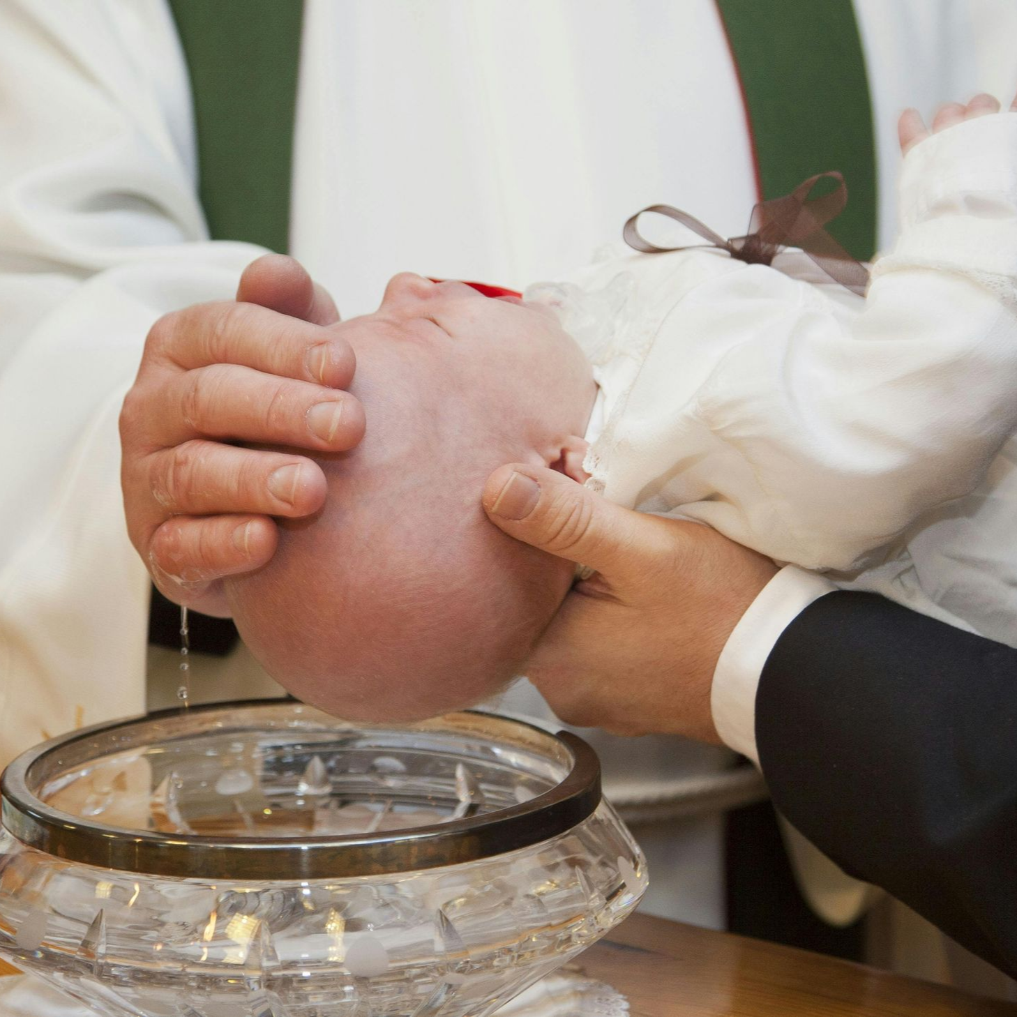 A baby is cradled in a man's hand during a baptism.