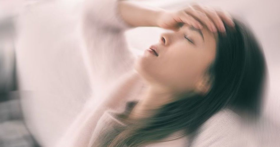 A dizzy woman is laying on a bed with her hand on her forehead.