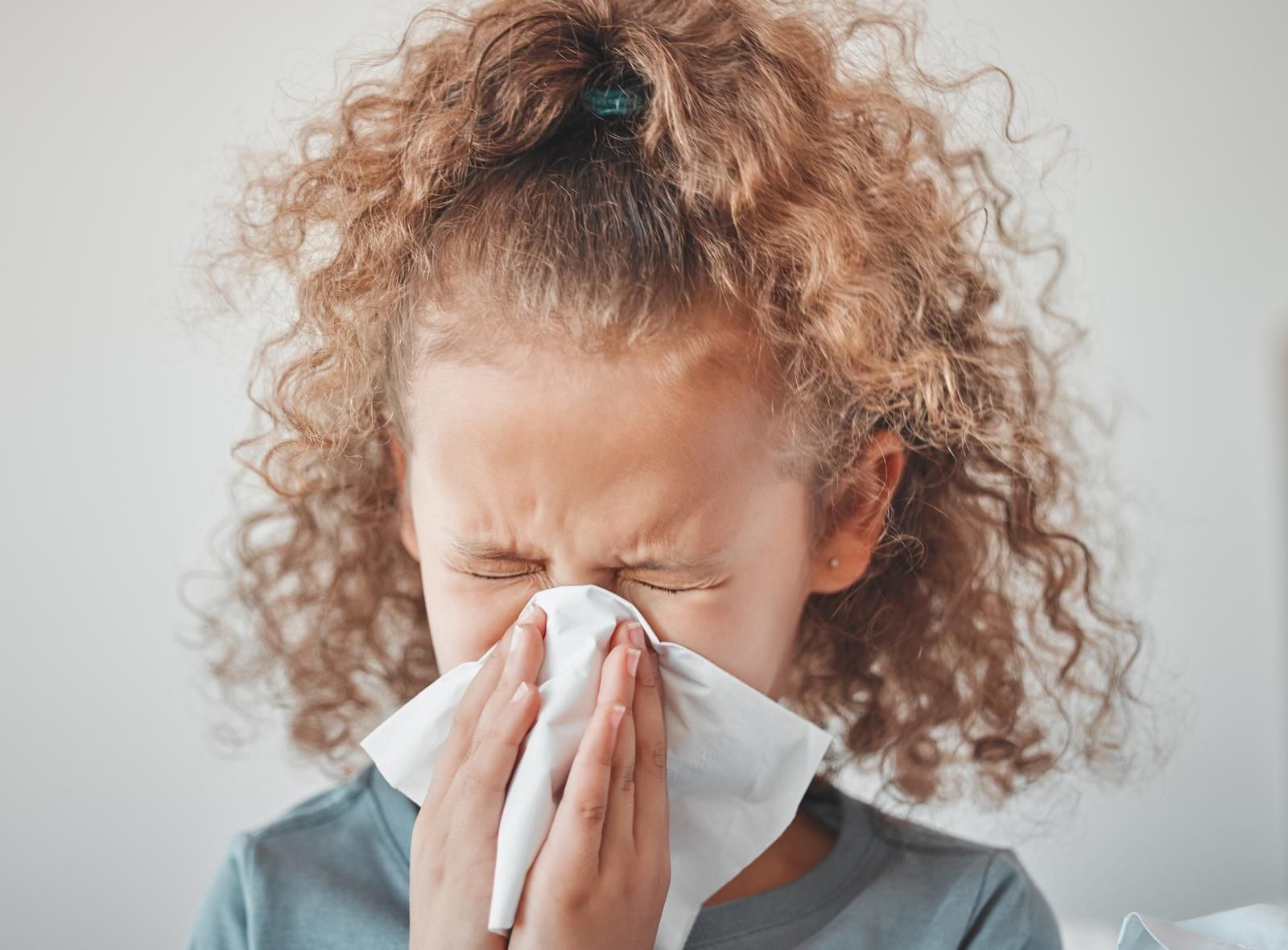 A little girl is blowing her nose into a napkin.