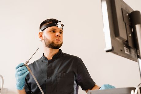 A man is holding a surgical instrument in front of a computer monitor.
