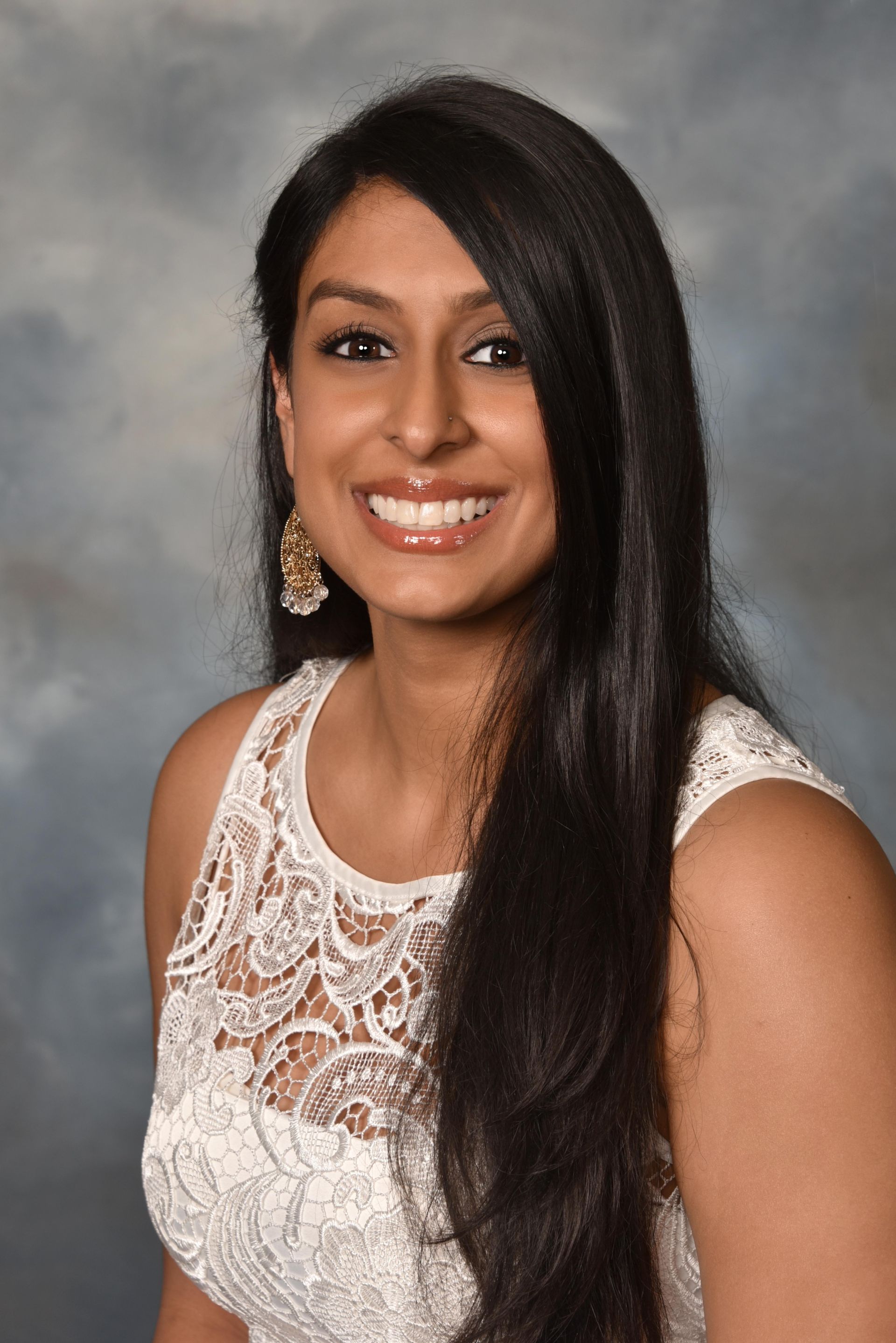 A woman with long black hair is wearing a white lace top and smiling for the camera.