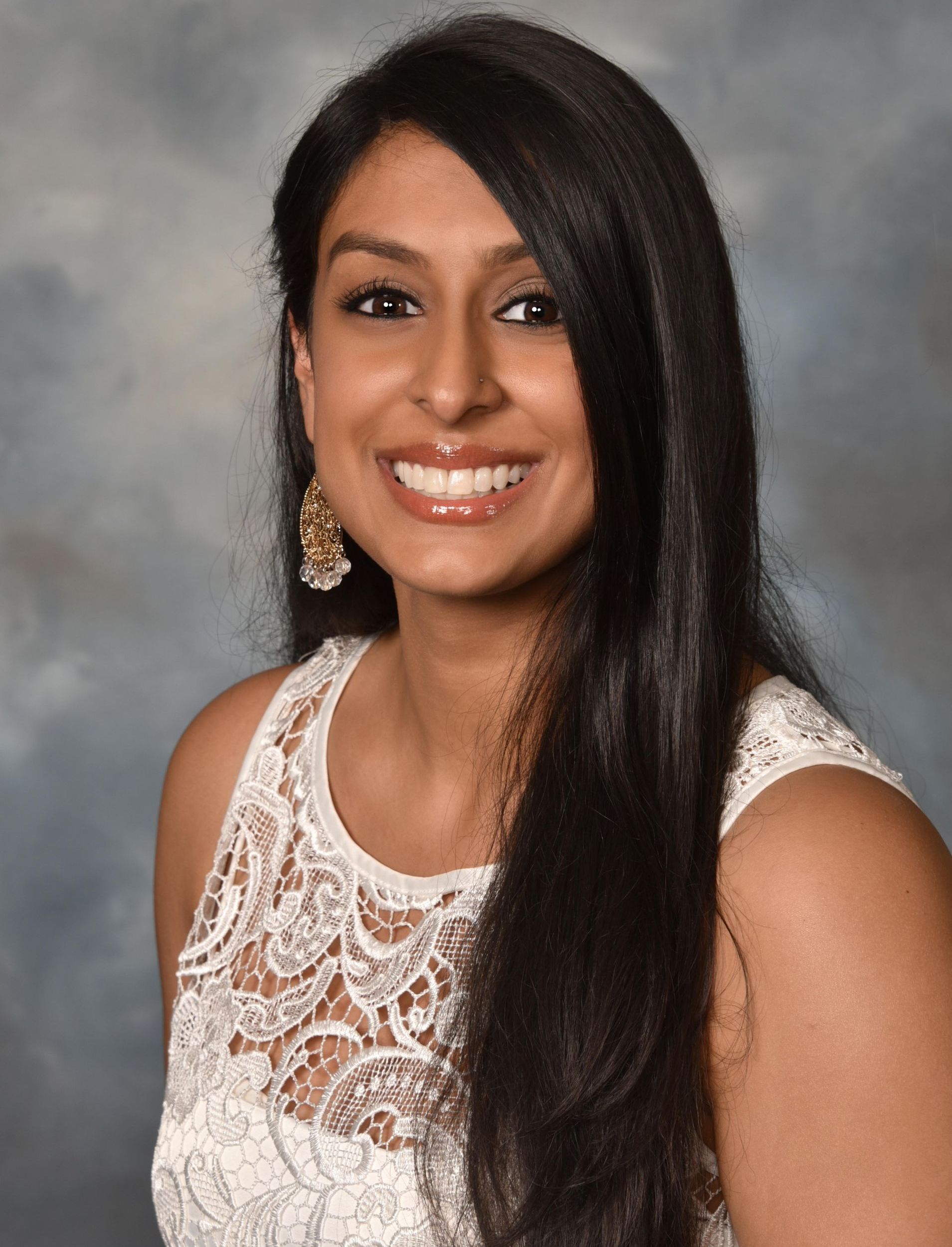 A woman with long black hair is wearing a white lace top and smiling.