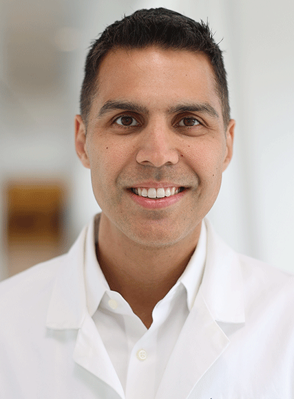 A man in a white lab coat is smiling for the camera.