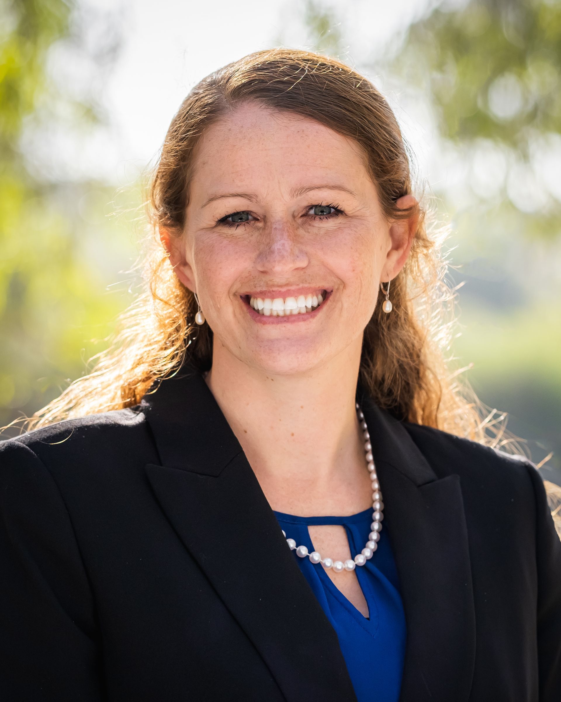 A woman in a blue shirt and black jacket is smiling for the camera.