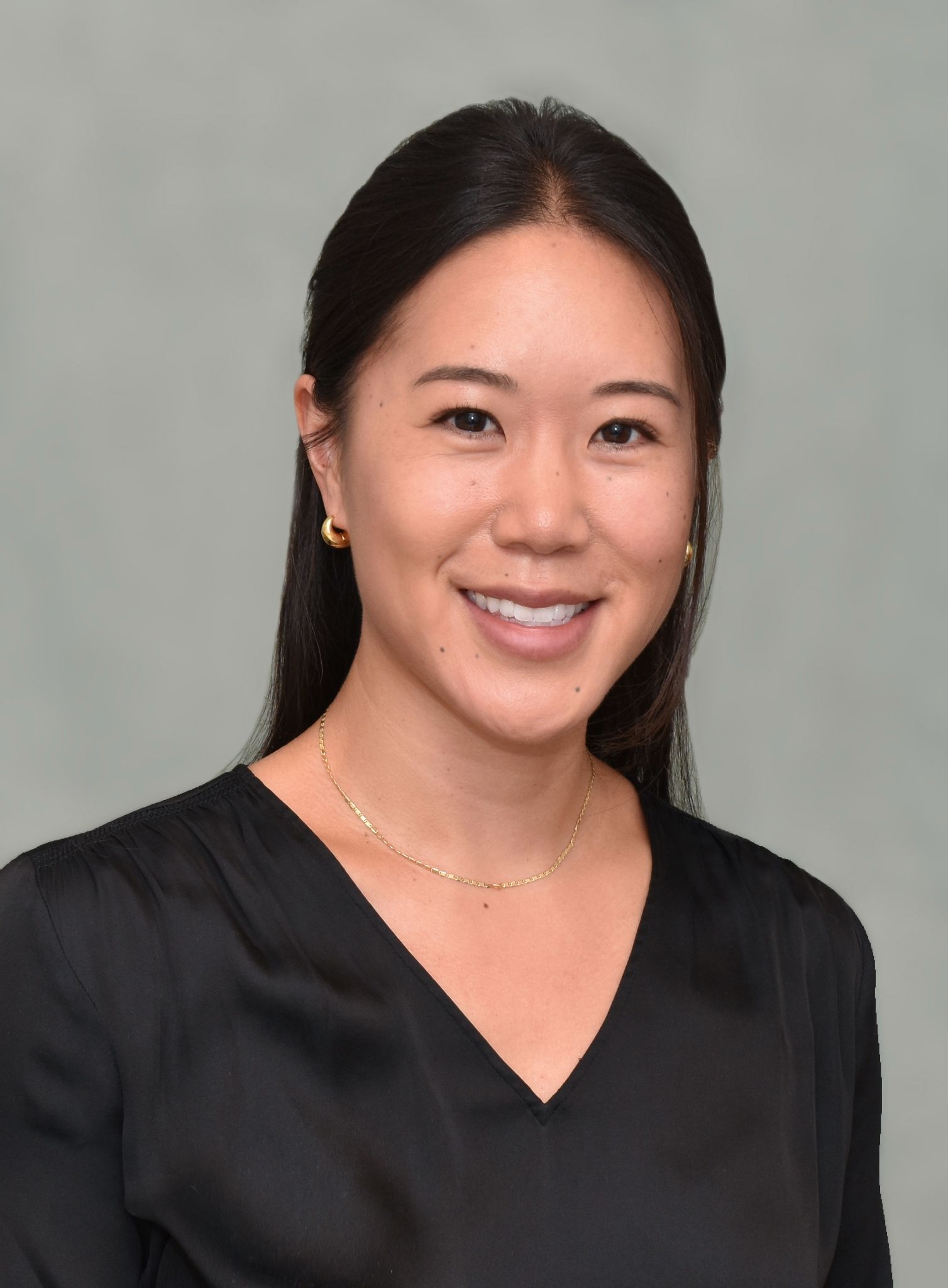 A woman in a blue shirt and black jacket is smiling for the camera.