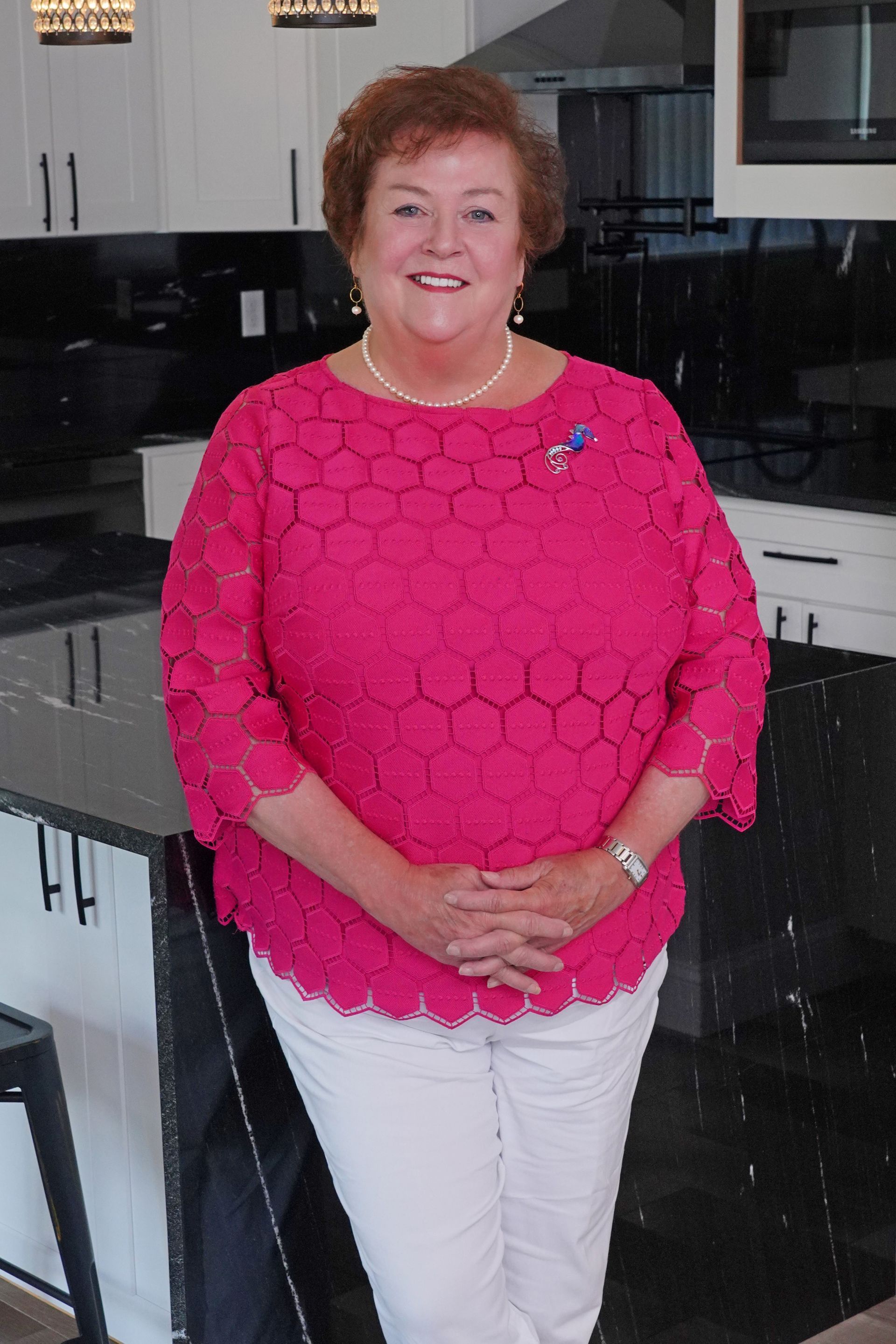 A woman in a pink top and white pants is standing in a kitchen