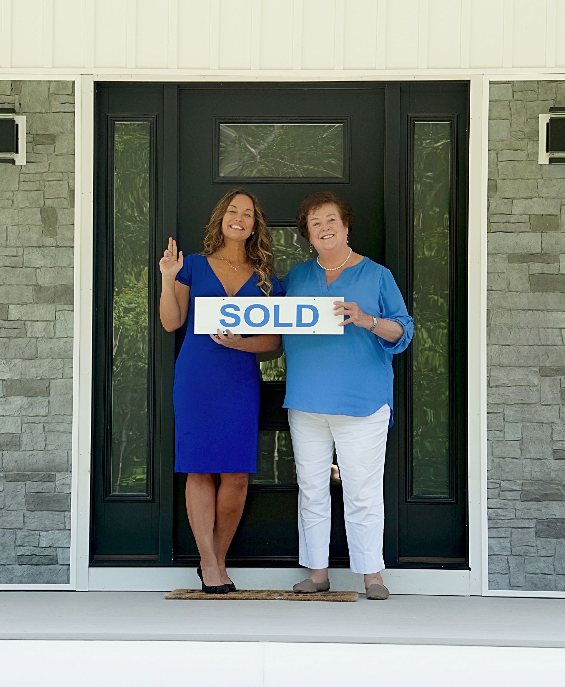 Two women standing in front of a house holding a sold sign
