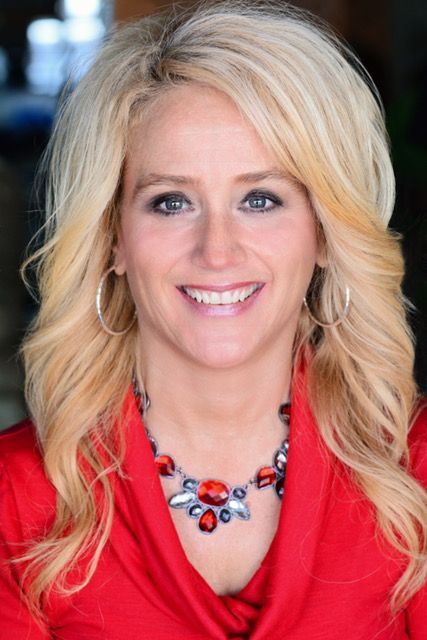 A woman wearing a red shirt and a necklace smiles for the camera.