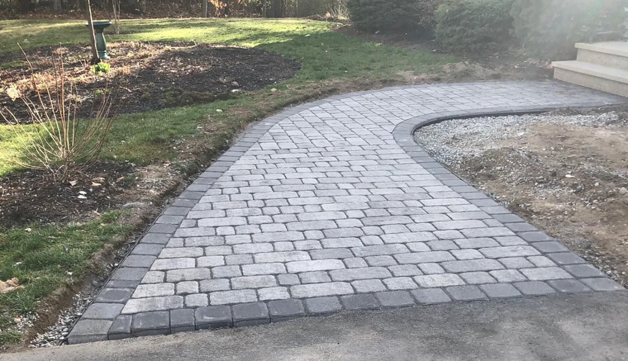 Curved light-gray stone paver walkway beside a garden and steps at the top right