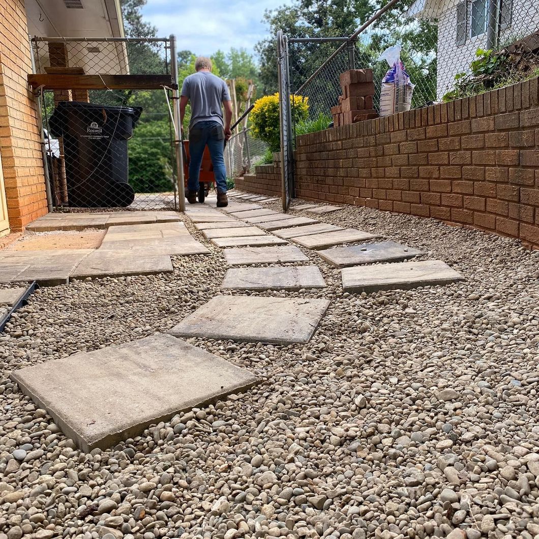 A person walks along a stepping stone path through a gravel yard beside a brick house and retaining wall. A person walks along a stepping stone path through a gravel yard beside a brick house and retaining wall.