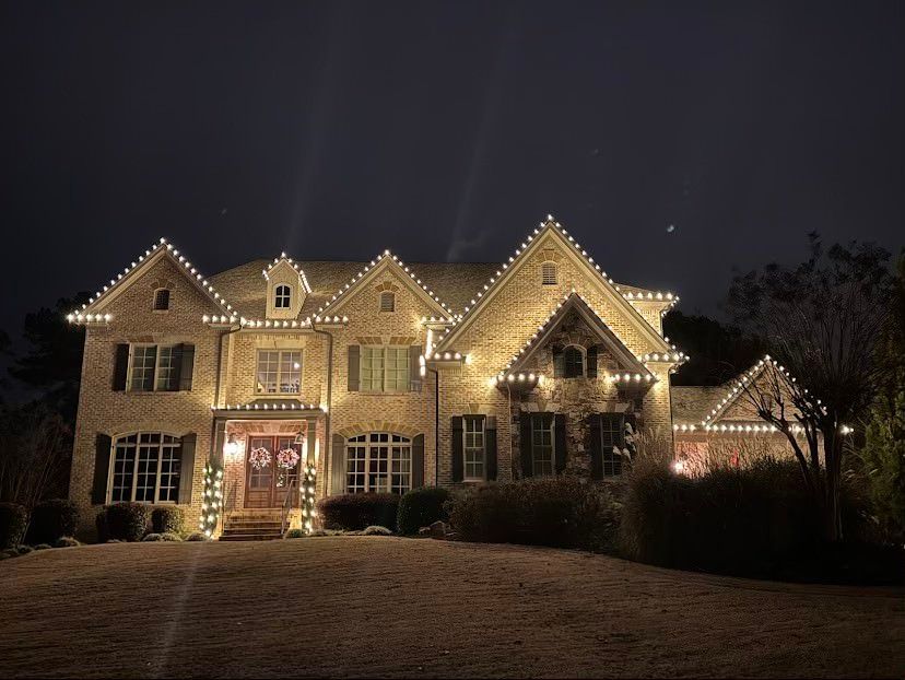 A residential home at night decorated with numerous glowing Christmas lights, icicle lights, and a white picket fence. A residential home at night decorated with numerous glowing Christmas lights, icicle lights, and a white picket fence.
