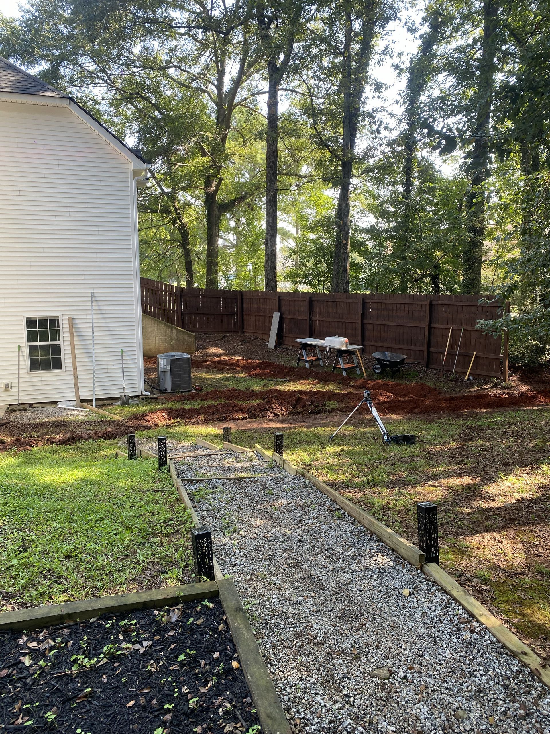 Gravel path leading to a white house and fenced backyard with trees and a small garden area