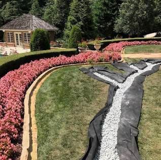 Curved pink flowerbeds beside a landscaped stone and gravel garden path with a gazebo and evergreens