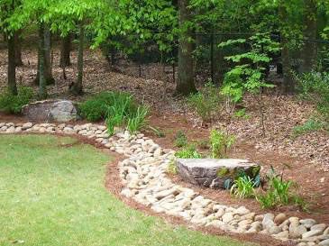 Curved stone border edging a green lawn beside a wooded garden bed and small concrete step.