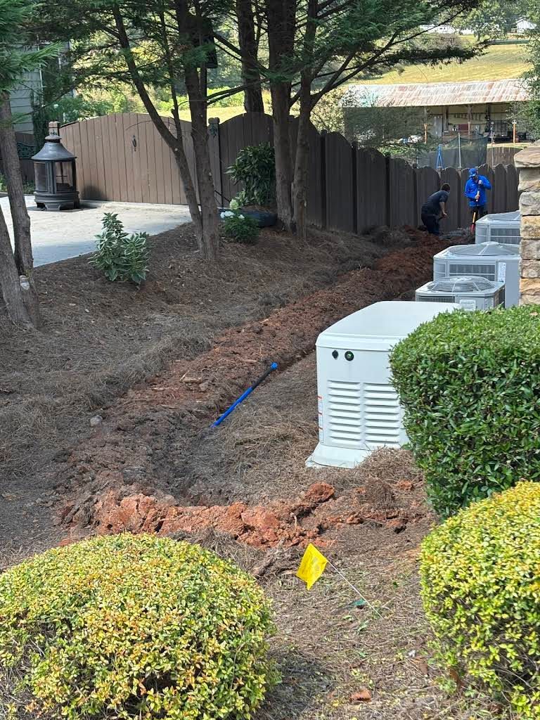 Workers in a landscaped yard installing or servicing two large, white outdoor standby generators near a wooden fence.
