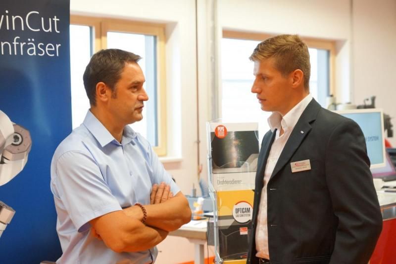Zwei Männer unterhalten sich vor einem Schild mit der Aufschrift „Vincut“