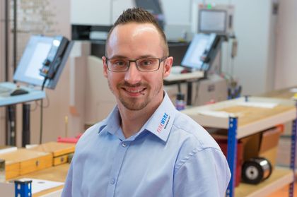 Ein Mann mit Brille und blauem Hemd steht in einer Lagerhalle.