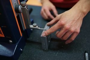 Eine Person verwendet eine Maschine, um ein Stück Metall zu messen.
