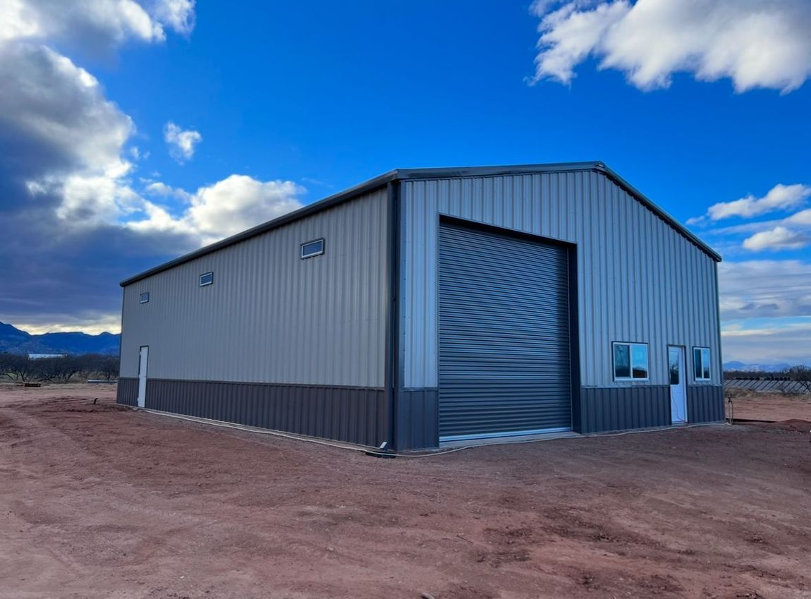 A large metal building with a large garage door is sitting in the middle of a dirt field.