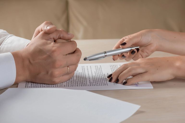 Mani che firmano un documento a una scrivania, con una penna tenuta sopra la documentazione.