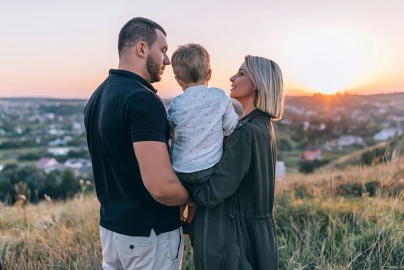 Una coppia con un bambino in braccio su una collina al tramonto, con vista sulla città.